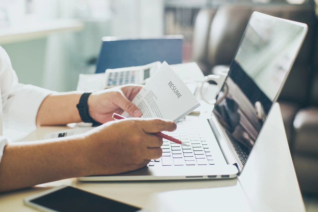 A person is holding a paper and typing on a laptop.